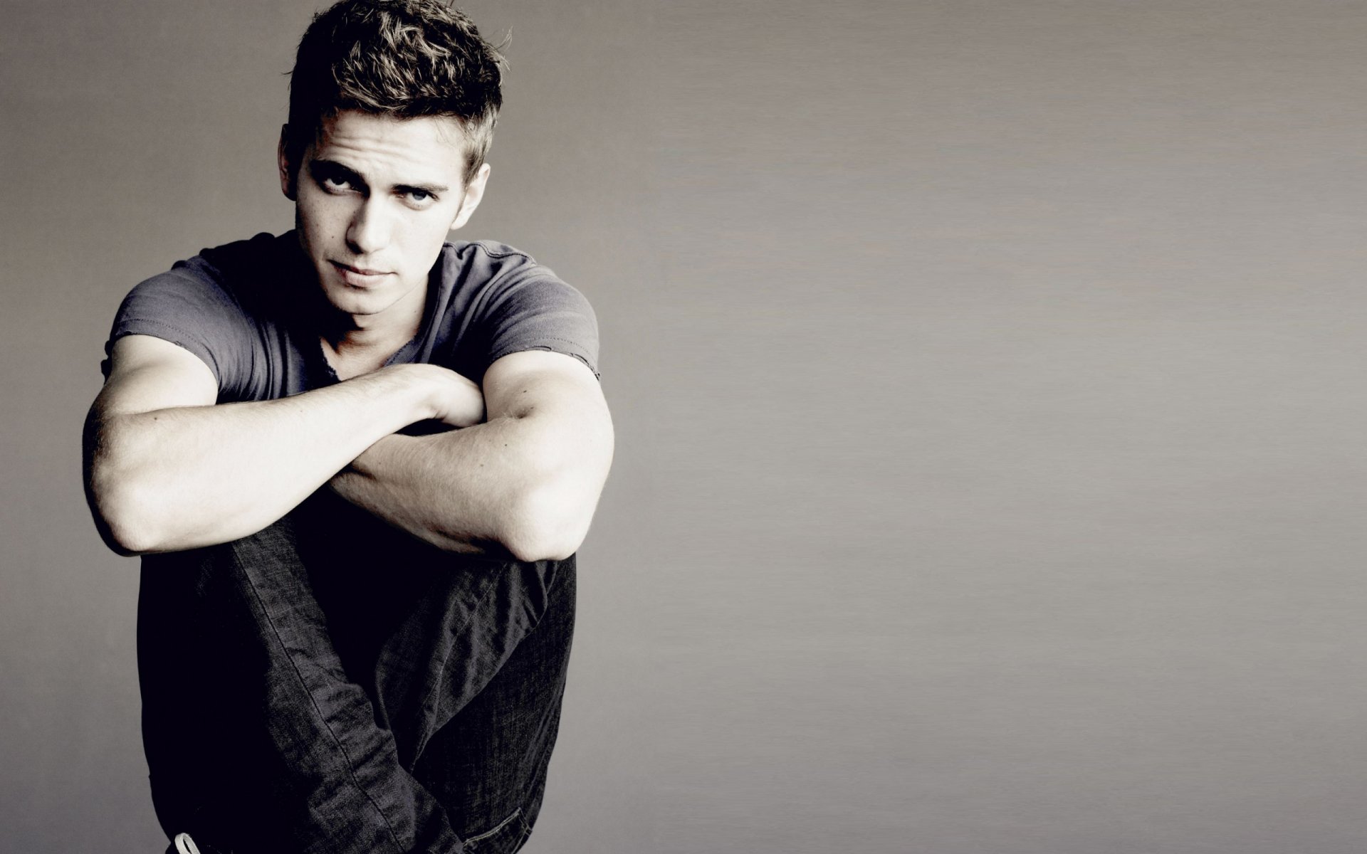 HD PC desktop wallpaper featuring celebrity Hayden Christensen sitting with arms crossed over his knees against a neutral gray background.