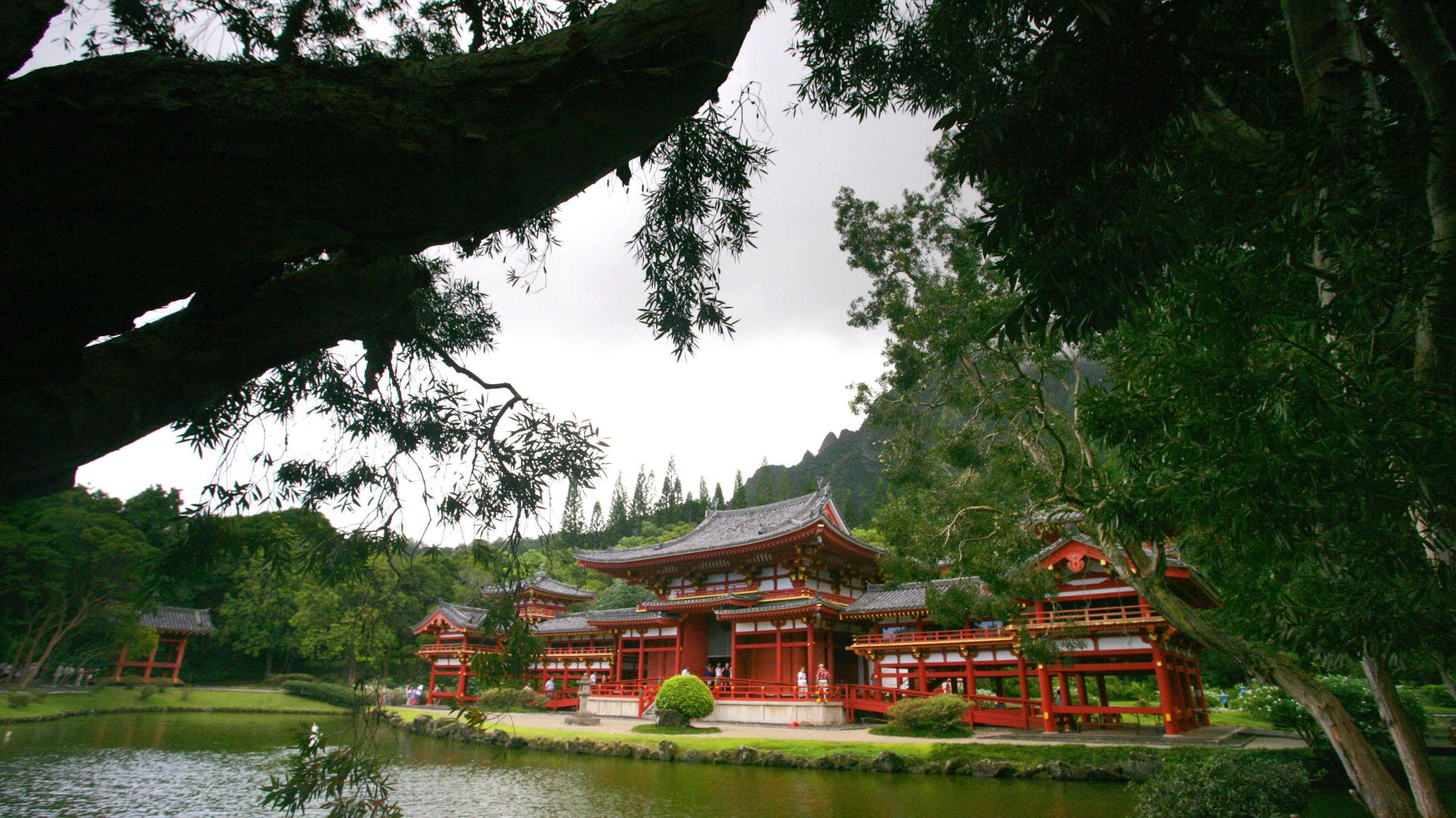 HD desktop wallpaper: Byodo-In temple, red wooden religious shrine beside a reflective pond, framed by trees with a mountain backdrop.