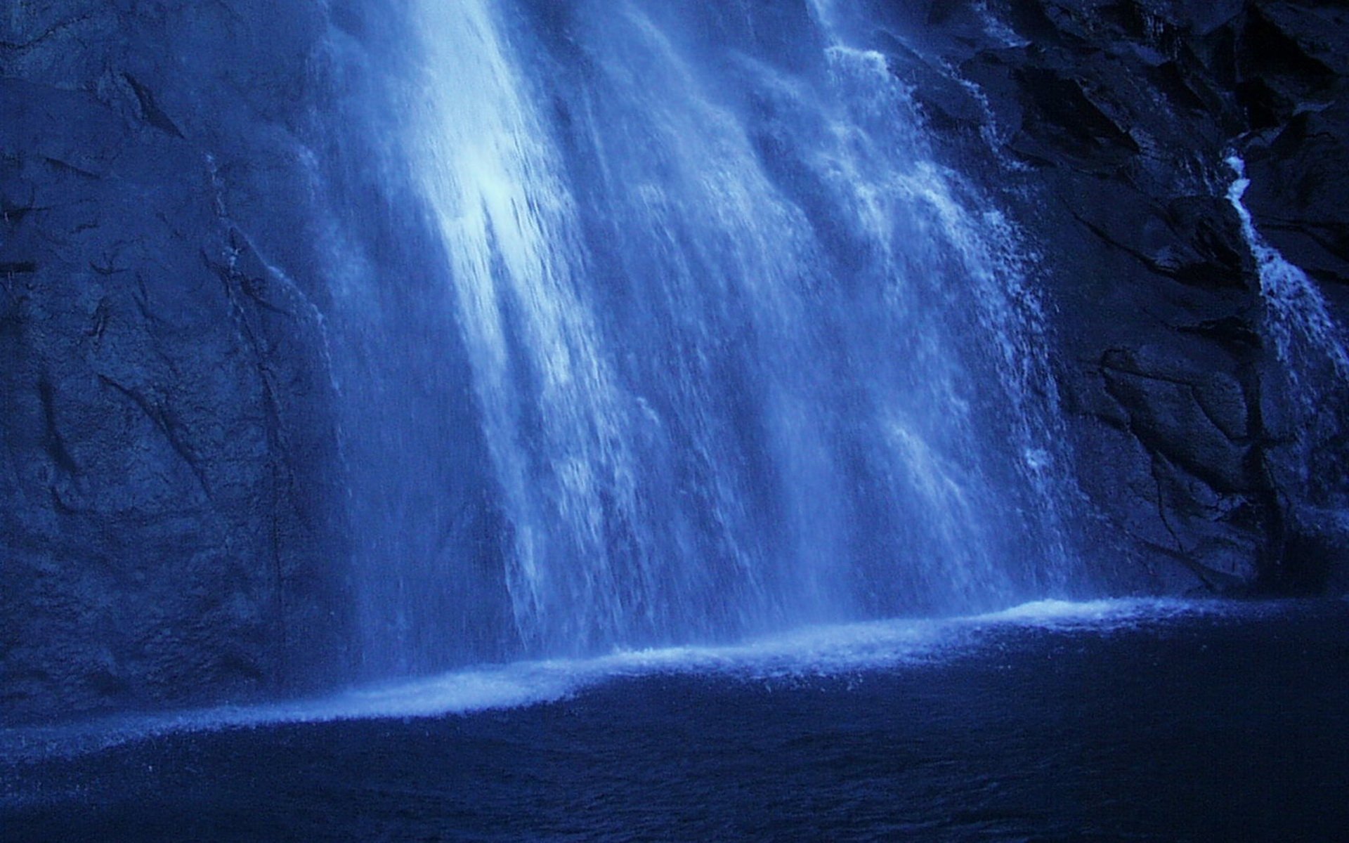 HD PC desktop wallpaper/background: nature scene of a blue-lit waterfall cascading into a dark pool at the base of rocky cliffs.