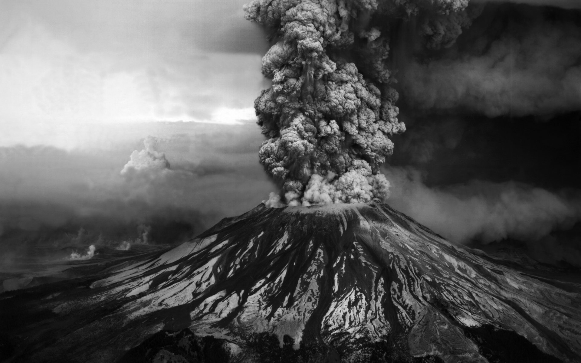 HD desktop wallpaper showing Mount St. Helens erupting, with thick smoke and ash clouds rising above the volcano amid a dramatic natural landscape.