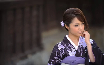 HD wallpaper of an Asian woman in a traditional oriental outfit, adorned with a delicate hair accessory. She is standing thoughtfully with a blurred dark background.
