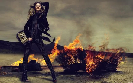 HD PC desktop wallpaper featuring celebrity Gisele Bündchen standing confidently in front of a blazing fire under a dramatic, cloudy sky.