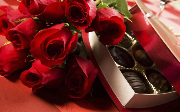 A romantic Valentine's Day scene features vibrant red roses beside a box of assorted chocolates, set against a warm, red background, creating an inviting holiday atmosphere.