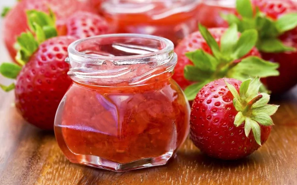 HD PC desktop wallpaper featuring a close-up of a small jar of strawberry jam surrounded by fresh strawberries on a wooden surface.
