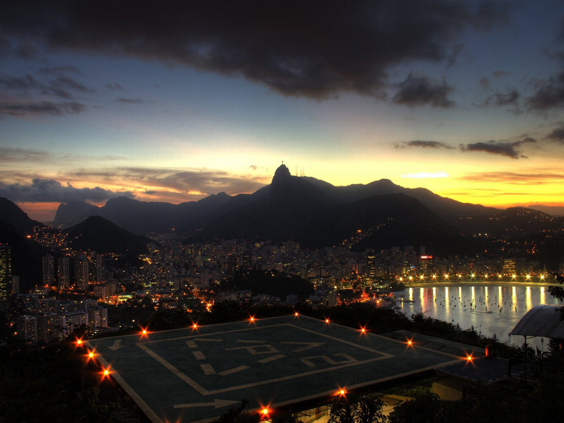 HD PC desktop wallpaper and background: Rio de Janeiro at dusk, illuminated man-made helipad and waterfront, city lights and mountain silhouettes under a colorful sky.