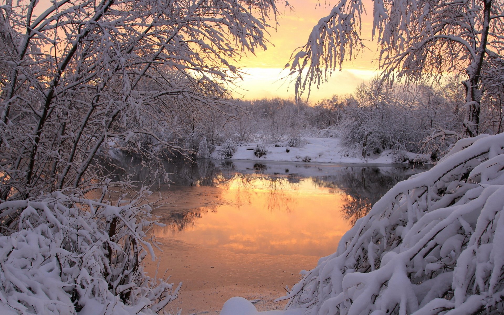 HD PC desktop wallpaper showing a serene winter landscape with snow-covered trees reflecting in a calm river under a golden sunset sky.