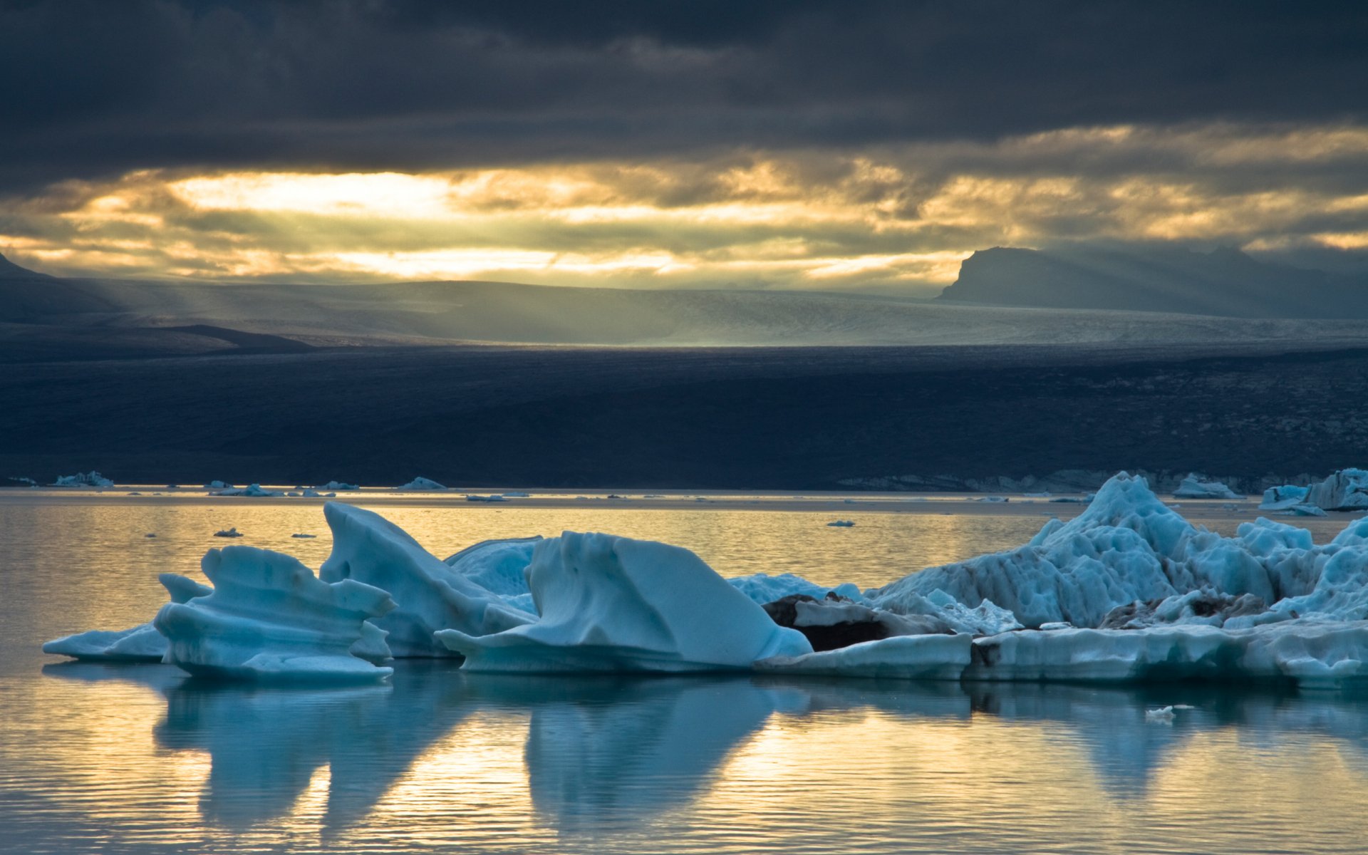 2K Quad HD PC desktop wallpaper: nature scene of icebergs floating on glassy water beneath a dramatic, cloud-lit golden sky.