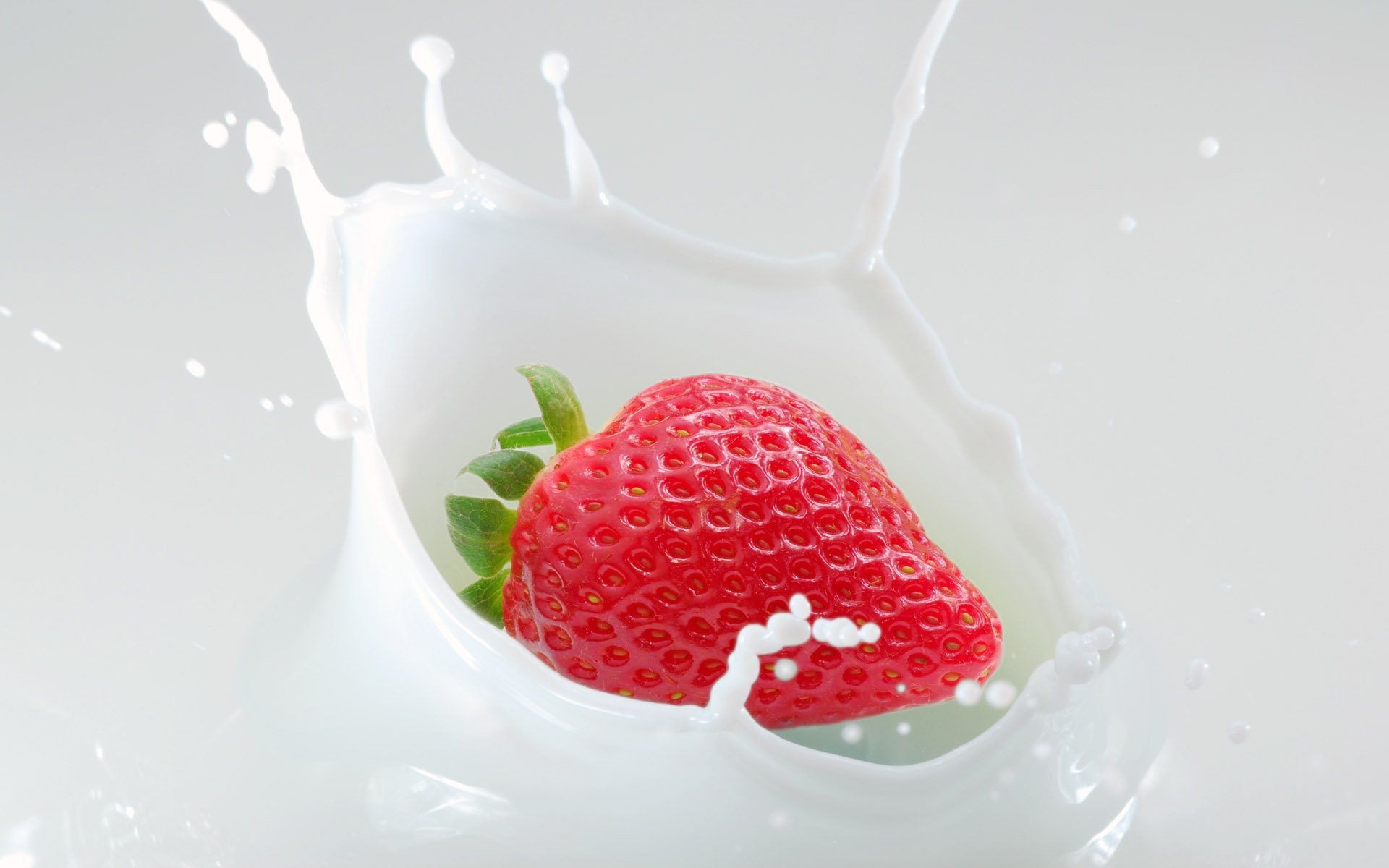 HD desktop wallpaper featuring a fresh strawberry splashing into creamy milk, highlighting vibrant food colors and dynamic motion.