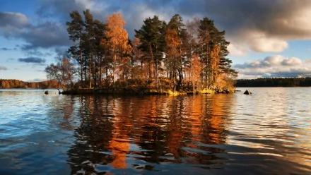 HD PC desktop wallpaper and background: tranquil nature island with autumn trees on a small isle, golden foliage reflecting in calm lake water under a dramatic sky.