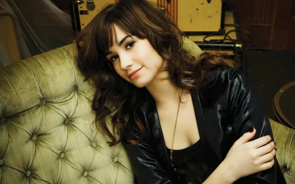 Demi Lovato poses comfortably on a stylish green couch, embodying her musical artistry. This HD wallpaper captures her charming personality in a vibrant setting.