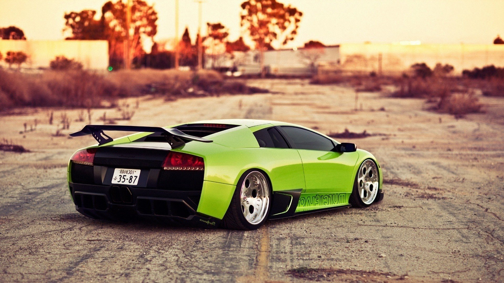HD PC desktop wallpaper showcasing a vibrant green Lamborghini Murcielago parked on a dusty road with a warm, golden sunset background.