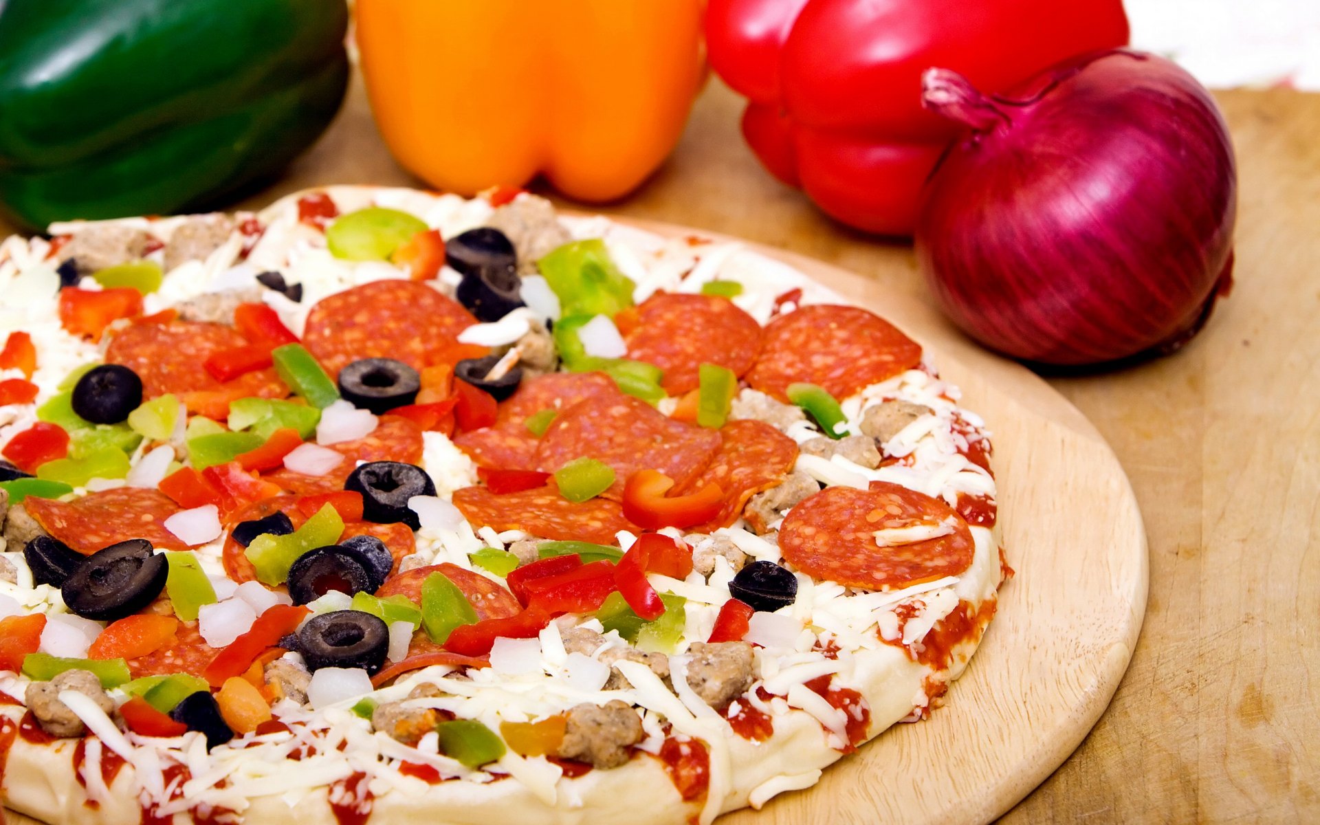 2K Quad HD PC desktop wallpaper background: food — a colorful pizza with pepperoni, black olives, diced bell peppers and red onion on a wooden board.