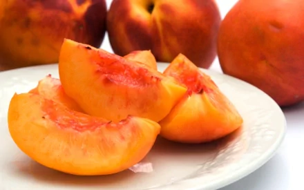 HD PC desktop wallpaper and background showing a close-up of sliced ripe peaches on a white plate with whole peaches blurred behind — food, peach