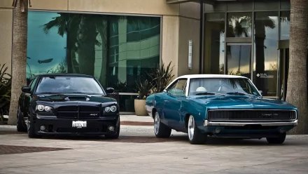 A sleek black Dodge Charger and a vintage blue Charger are parked side by side in front of a modern building, highlighting the contrast between classic and contemporary design.