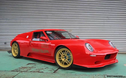 HD PC desktop wallpaper featuring a red Lotus Europa sports car with gold wheels parked in front of a gray corrugated metal wall.