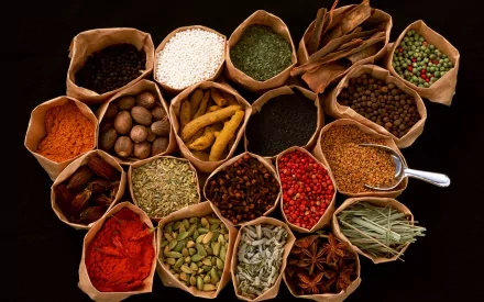 HD PC desktop wallpaper featuring an array of colorful herbs and spices arranged in small paper bags on a dark background, highlighting vibrant food ingredients.