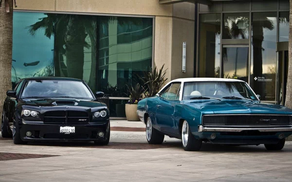 A sleek black Dodge Charger and a vintage blue Charger are parked side by side in front of a modern building, highlighting the contrast between classic and contemporary design.