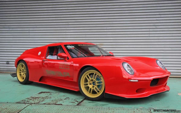 HD PC desktop wallpaper featuring a red Lotus Europa sports car with gold wheels parked in front of a gray corrugated metal wall.