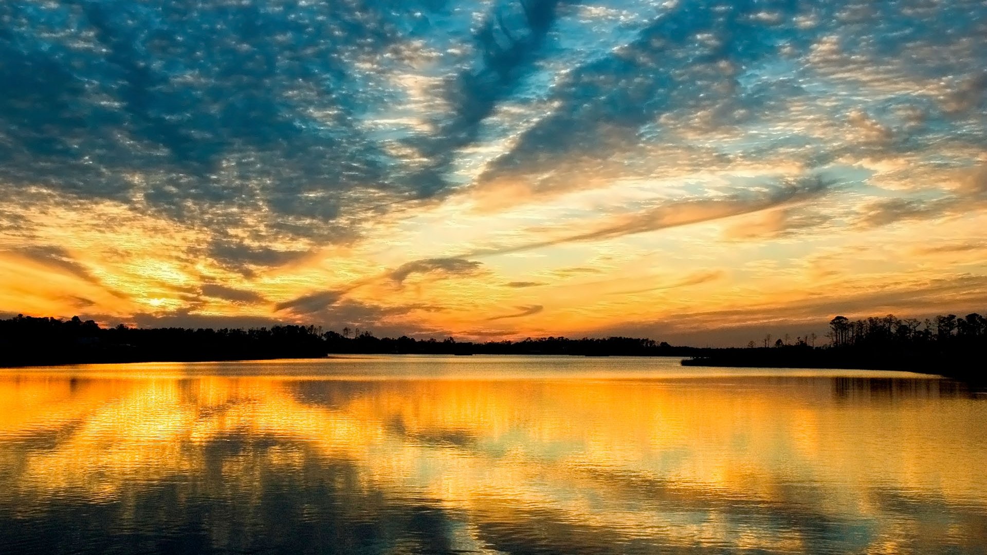 HD PC desktop wallpaper: golden sunset over a calm lake, dramatic cloud-filled sky mirrored in glassy water — nature reflection across a tranquil horizon.