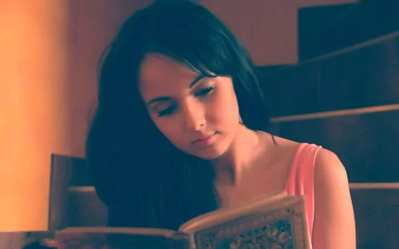 HD desktop wallpaper of an artistic woman with dark hair reading a book in a softly lit, warm-toned setting.