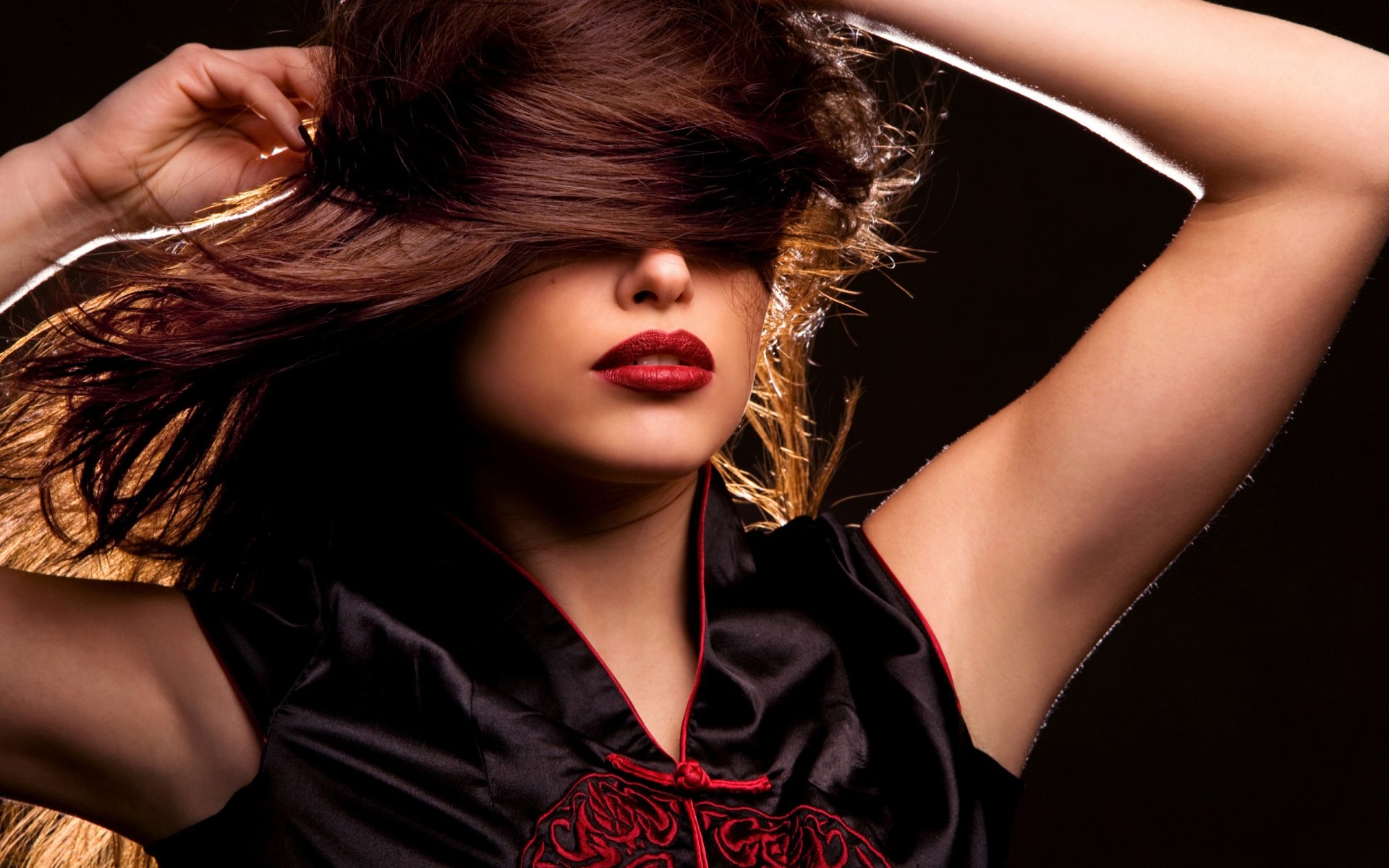 Close-up of a woman with dark hair swept across her face, red lips and raised arms — 2K Quad HD PC desktop wallpaper background.