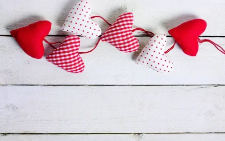 HD desktop wallpaper featuring a row of red and white patterned fabric hearts on a white wooden background, themed for Valentine's Day holiday.
