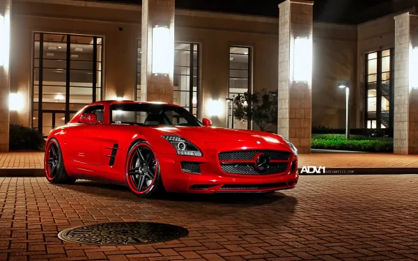 HD desktop wallpaper featuring a red Mercedes-Benz SLS AMG parked on a brick driveway in front of a modern building at night.