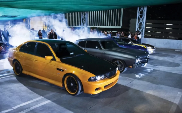 HD desktop wallpaper featuring iconic cars from the Fast & Furious movie franchise, set against a backdrop of smoke and excitement in a night scene.