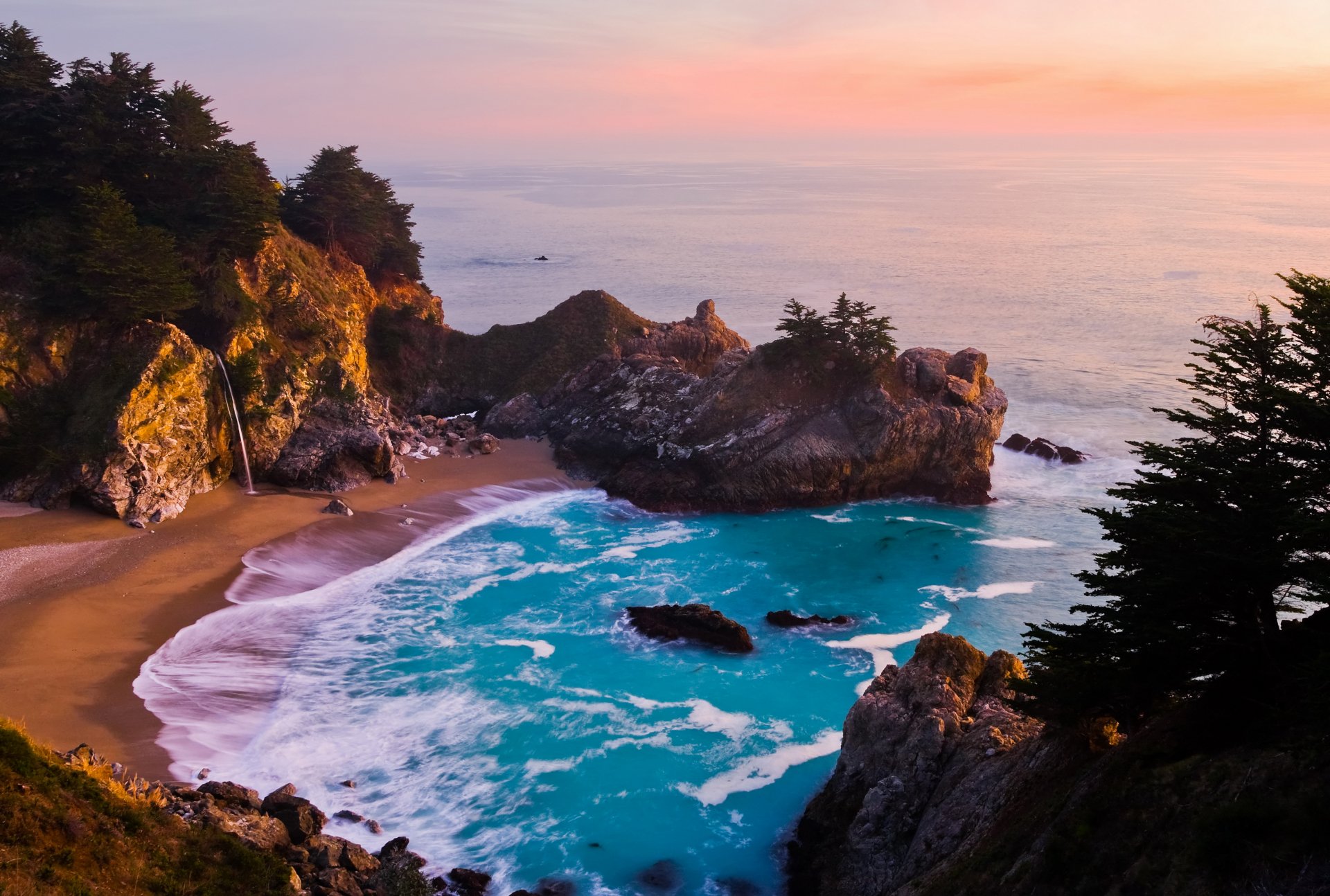 4K Ultra HD desktop wallpaper showcasing a serene coastline with rugged cliffs, turquoise waves, and a pastel sunset sky blending into the tranquil ocean.