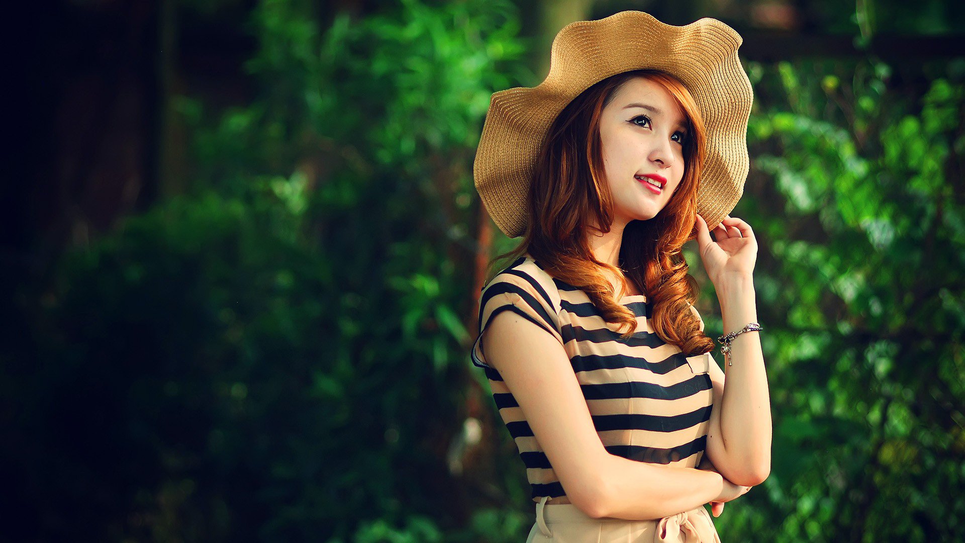 HD desktop wallpaper featuring an Asian woman in a striped shirt and floppy hat, posing against a lush, green background.
