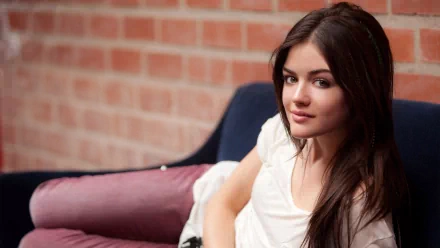 HD desktop wallpaper featuring celebrity Lucy Hale, relaxing on a couch against a brick wall background.