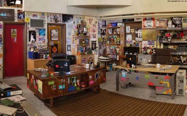 HD wallpaper of the iconic, cluttered office from the TV show The IT Crowd, featuring desks, computers, and walls covered in paraphernalia.