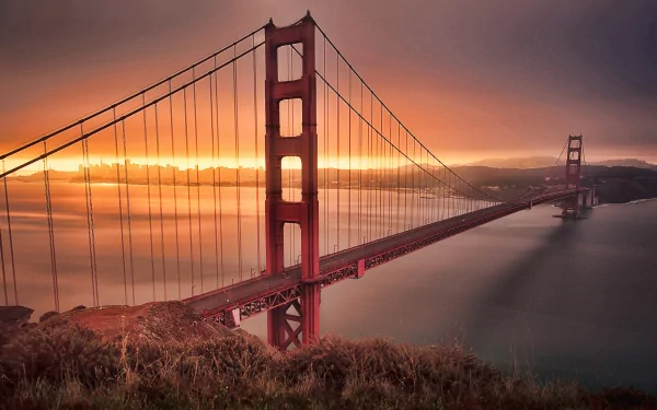 HD desktop wallpaper showcasing the iconic man-made Golden Gate Bridge glowing at sunset over calm waters with a dramatic sky.