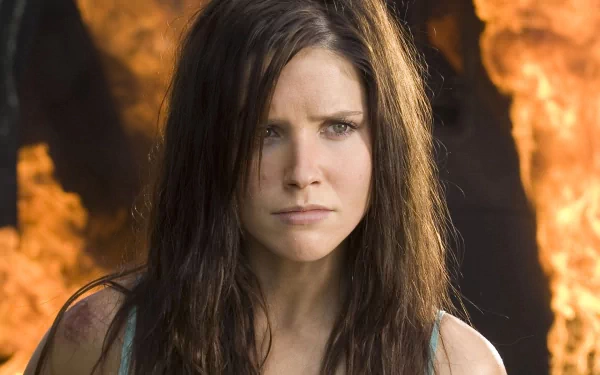 HD PC desktop wallpaper of a celebrity actress with long dark hair and a serious expression, standing in front of a dramatic, fiery background.