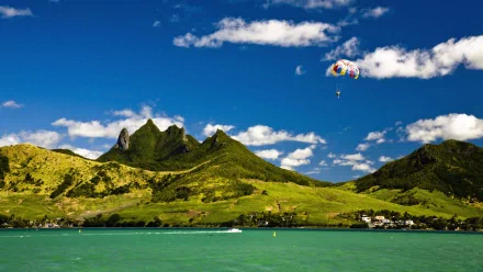 A skydiver descends with a colorful parachute over lush green mountains and a tranquil blue lagoon, capturing the thrill of sports in a stunning HD wallpaper.