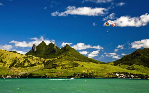 A skydiver descends with a colorful parachute over lush green mountains and a tranquil blue lagoon, capturing the thrill of sports in a stunning HD wallpaper.