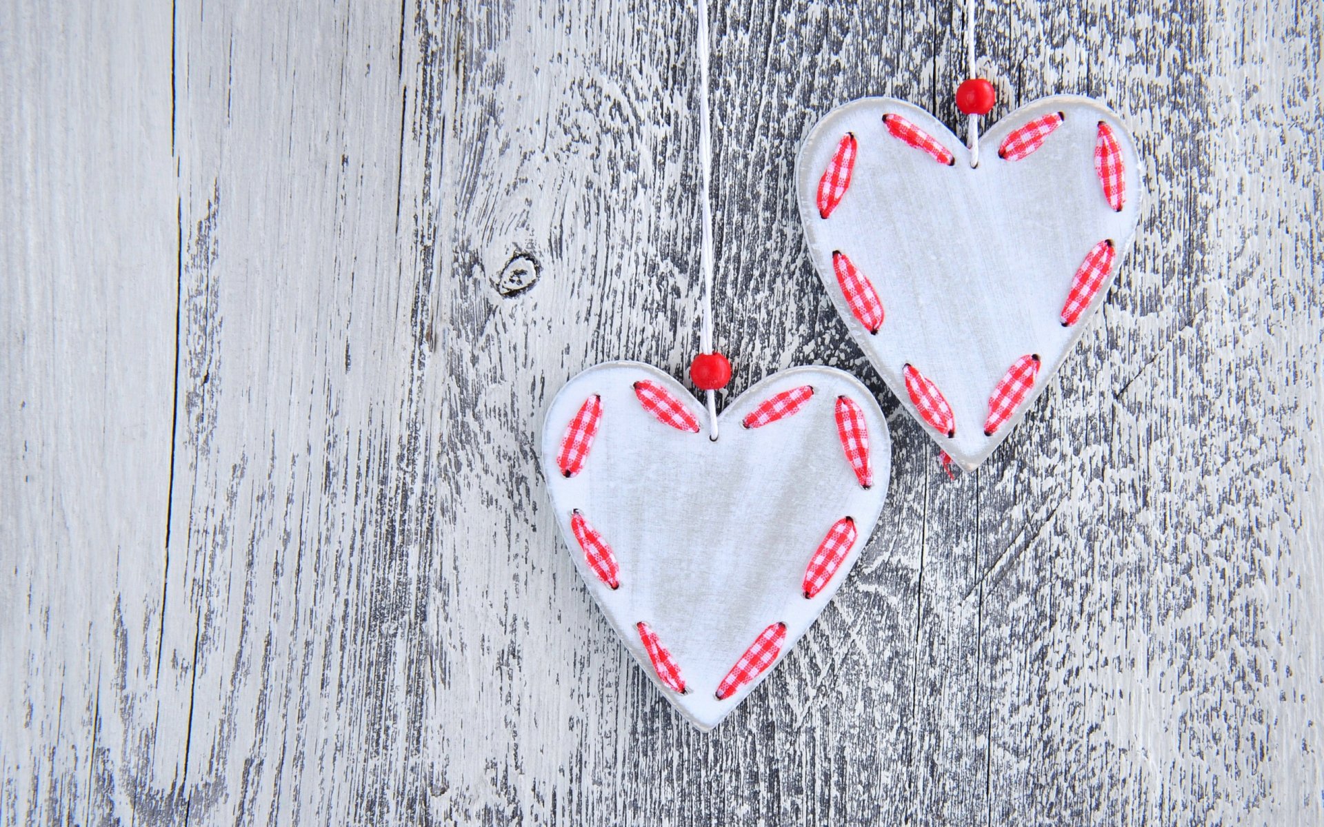 HD desktop wallpaper featuring two white heart ornaments with red stitching details on a rustic gray wooden background, celebrating Valentine's Day.