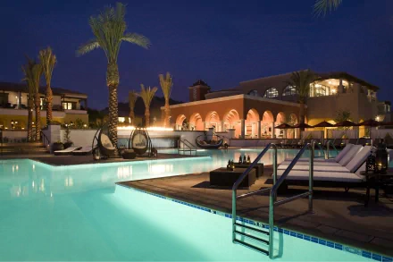 A luxurious mansion at night, featuring a shimmering pool and palm trees, creates a tranquil atmosphere, showcased in this stunning 4K Ultra HD desktop wallpaper.