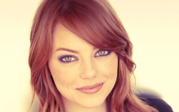A close-up portrait of Emma Stone, showcasing her vibrant red hair and captivating blue eyes, set against a soft background, designed as an HD desktop wallpaper.