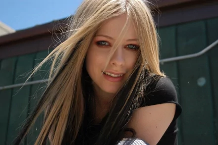 A vibrant HD desktop wallpaper featuring Avril Lavigne, showcasing her signature style with flowing hair and a bright smile against a sunny backdrop.