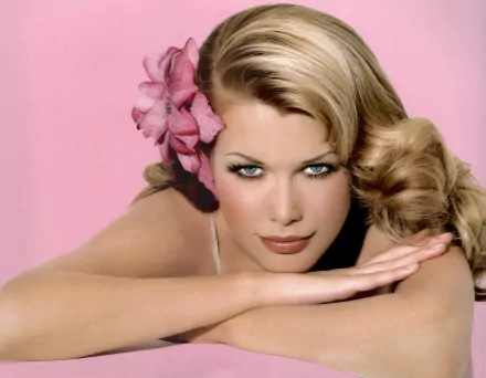 A close-up of Claudia Schiffer with elegant blonde hair and a pink flower, set against a soft pink background, serving as a striking HD desktop wallpaper.