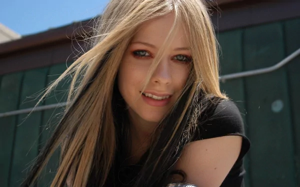 A vibrant HD desktop wallpaper featuring Avril Lavigne, showcasing her signature style with flowing hair and a bright smile against a sunny backdrop.