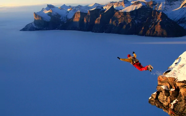 HD desktop wallpaper showing a skydiver in red gear leaping off a snowy cliff over a vast, cloud-covered mountain landscape, capturing the thrill of sports and adventure.