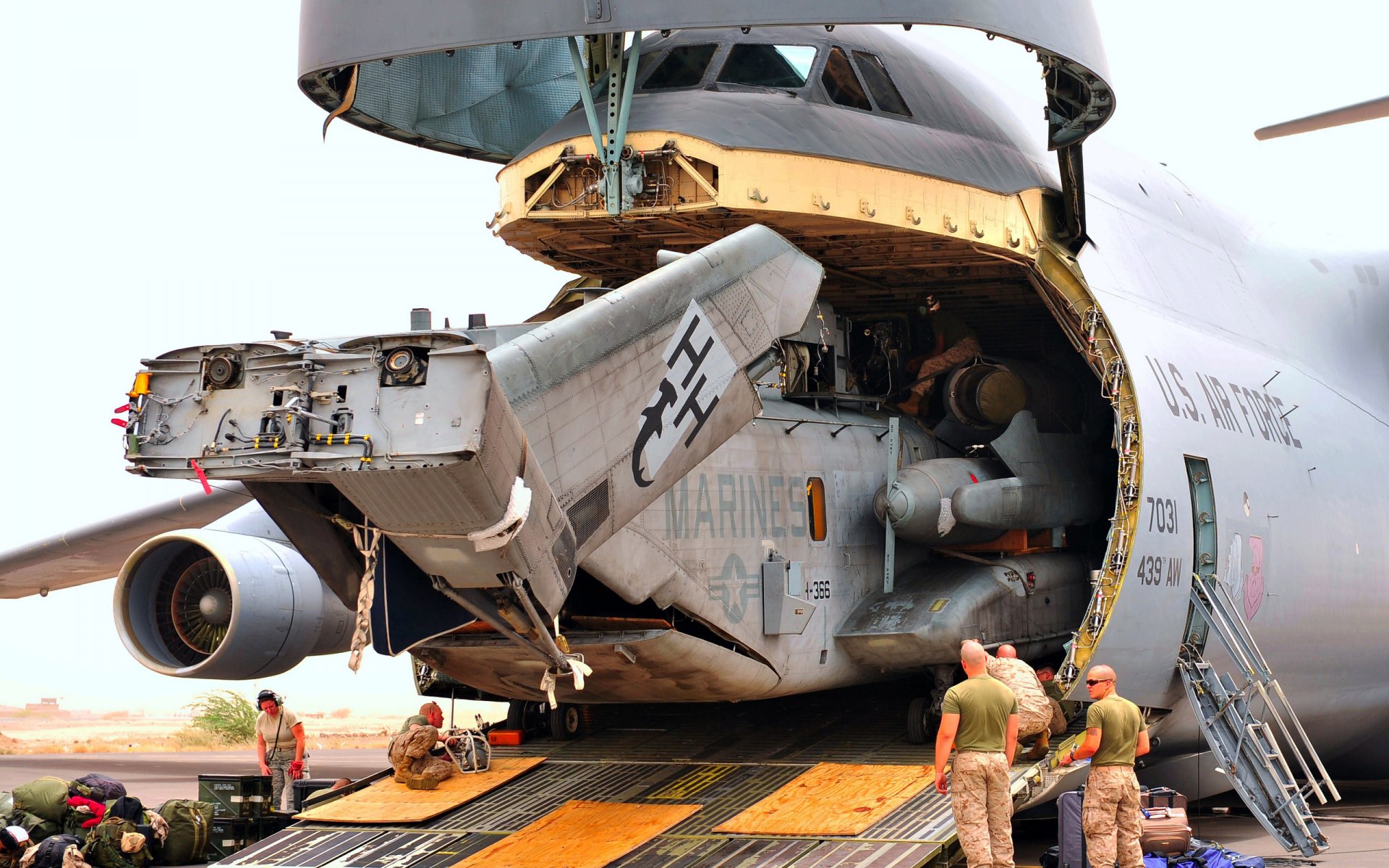 HD military desktop wallpaper featuring a Lockheed C-5 Galaxy cargo plane with its rear cargo door open and personnel loading equipment inside.