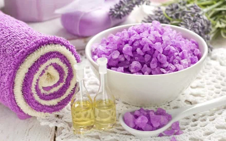 A serene spa scene featuring a bowl of purple bath salts, essential oils, and a rolled towel, all set against a soft, calming background for a relaxing desktop wallpaper.