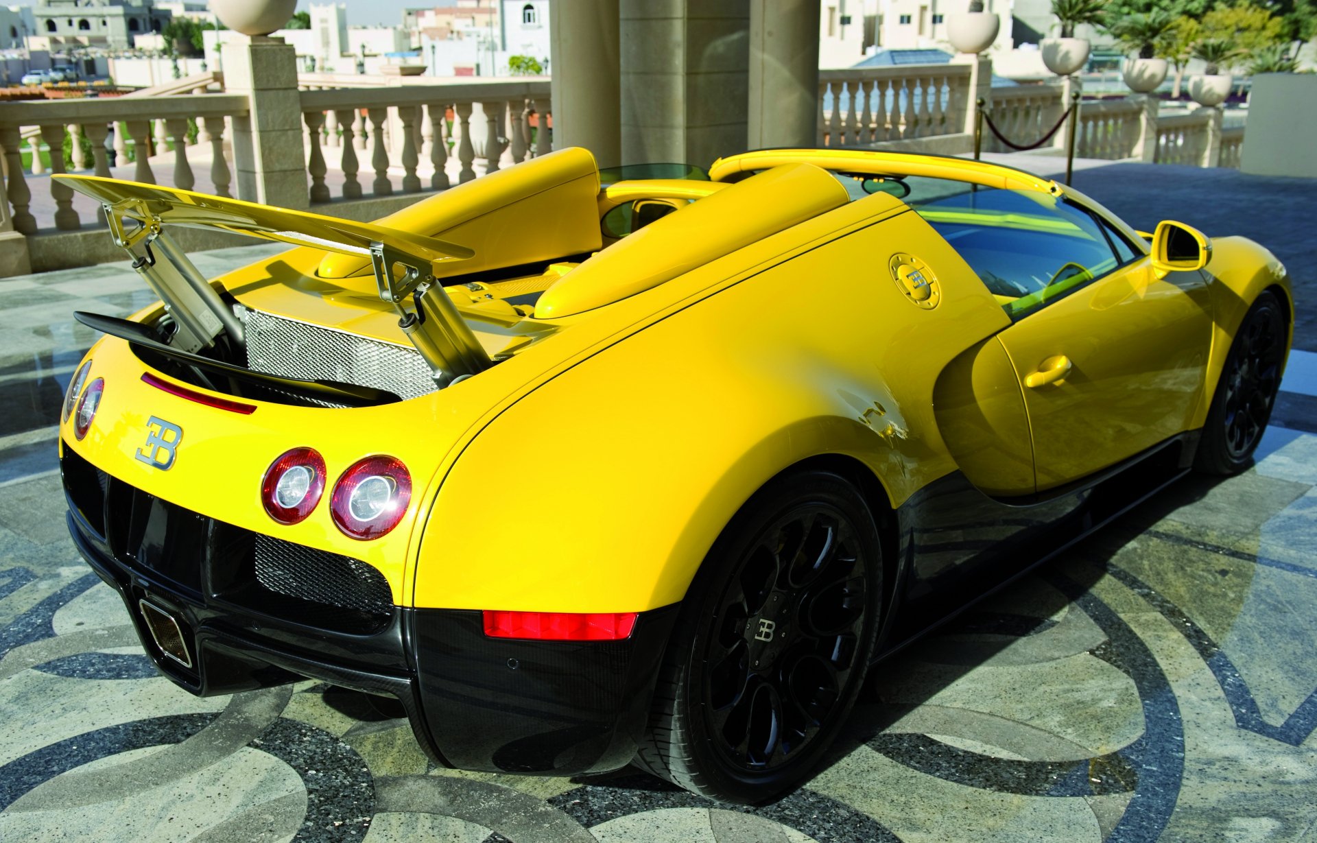 Bright yellow Bugatti Veyron sports car parked on an ornate terrace, 2K Quad HD PC desktop wallpaper/background.