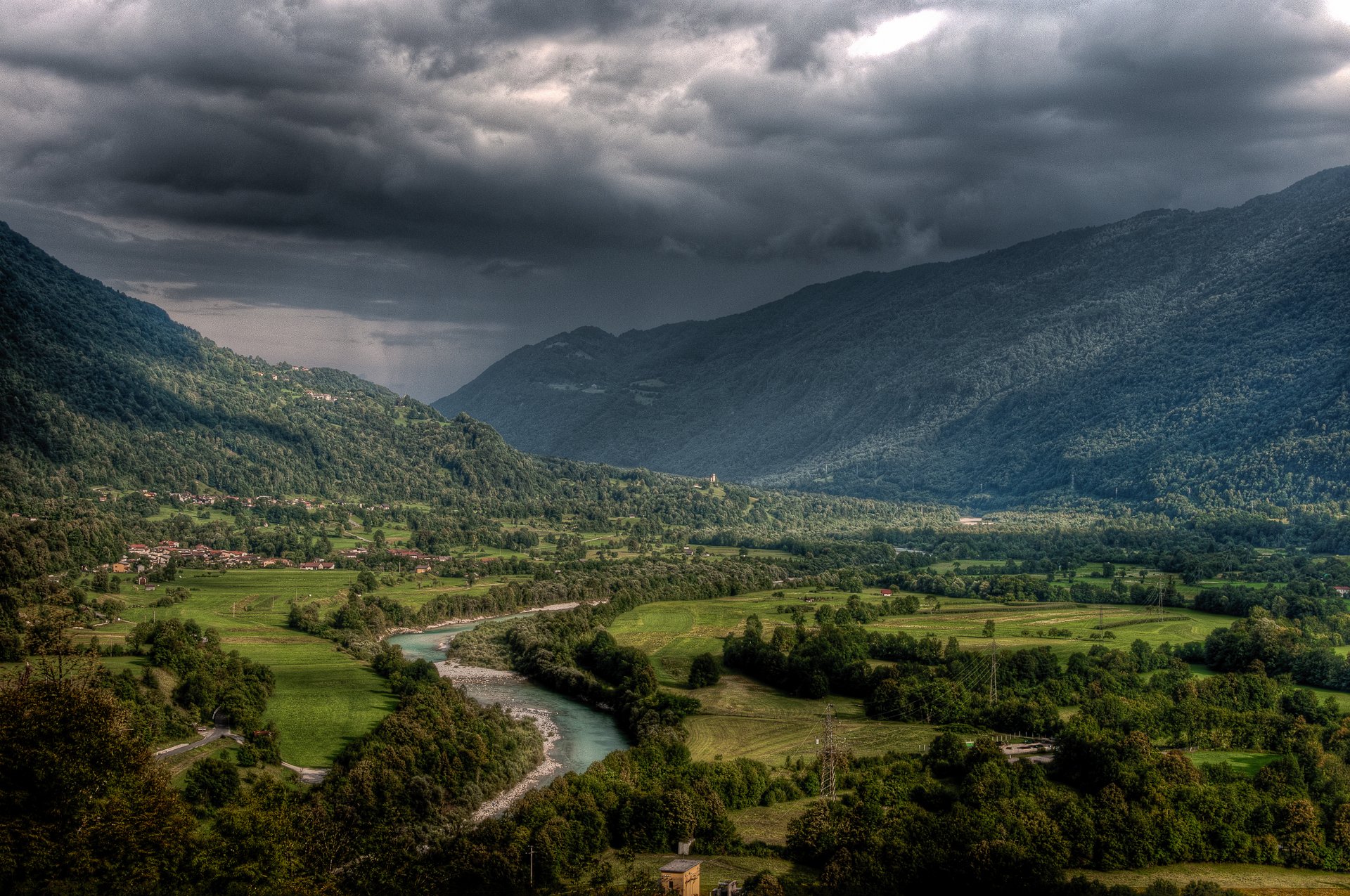Nature landscape HD PC desktop wallpaper/background: winding river through a lush green valley between forested mountains under brooding storm clouds.