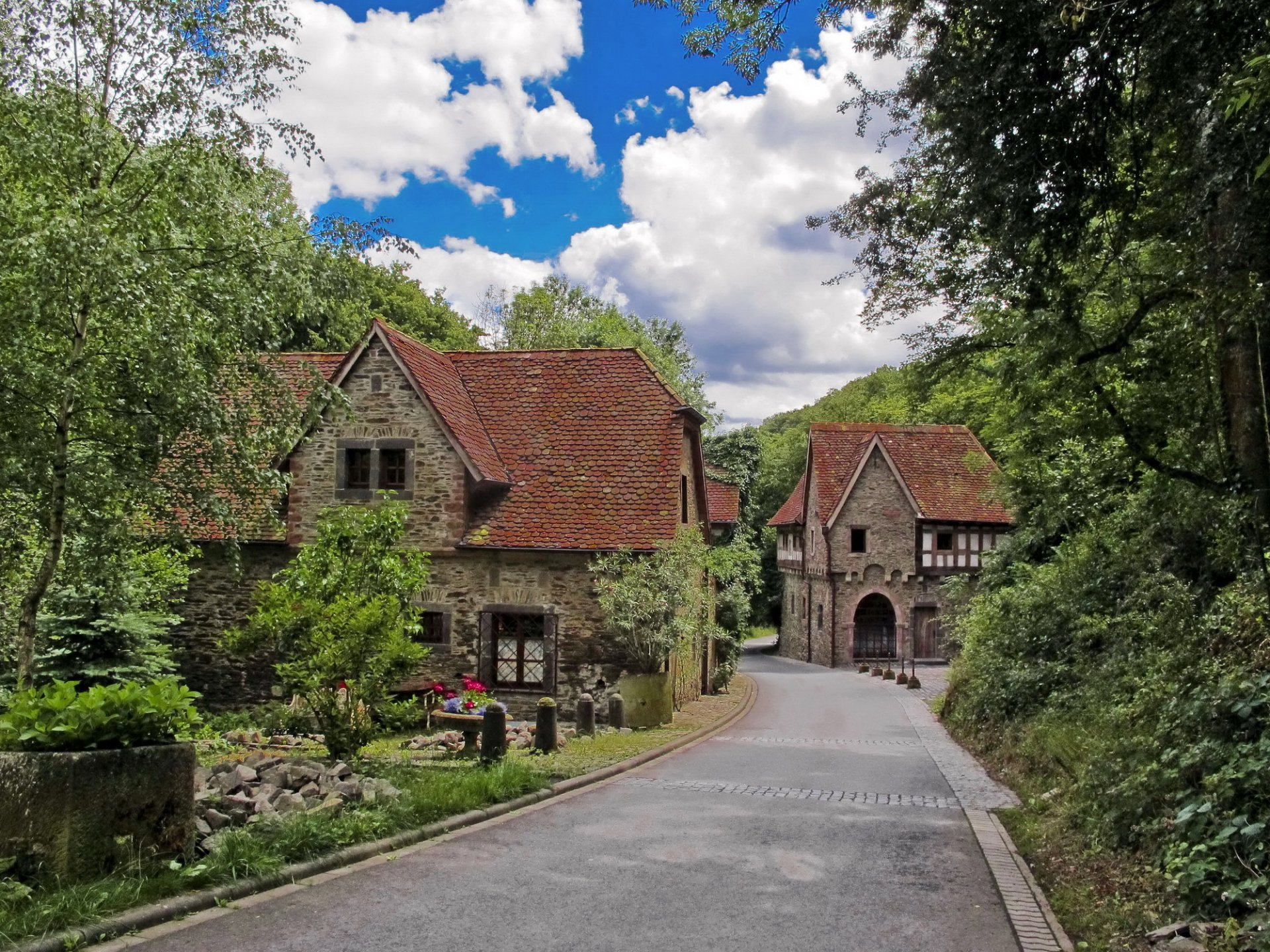 HD desktop wallpaper featuring charming stone houses in Kobern-Gondorf, Germany, surrounded by lush greenery and a clear blue sky.