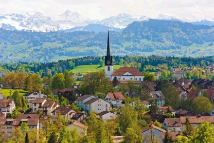 Panoramic HD desktop wallpaper featuring a Swiss village with charming houses, a prominent church, and mountainous backdrop under a clear sky.