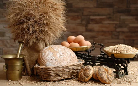 HD PC wallpaper showing a rustic food scene with a vintage scale, fresh eggs, round bread, and grains arranged on a wooden surface against a textured brick background.